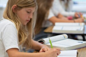 private school student sitting at classroom desk and writing down notes in Albany, NY