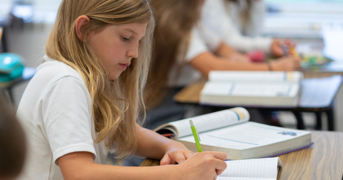 private school student sitting at classroom desk and writing down notes in Albany, NY