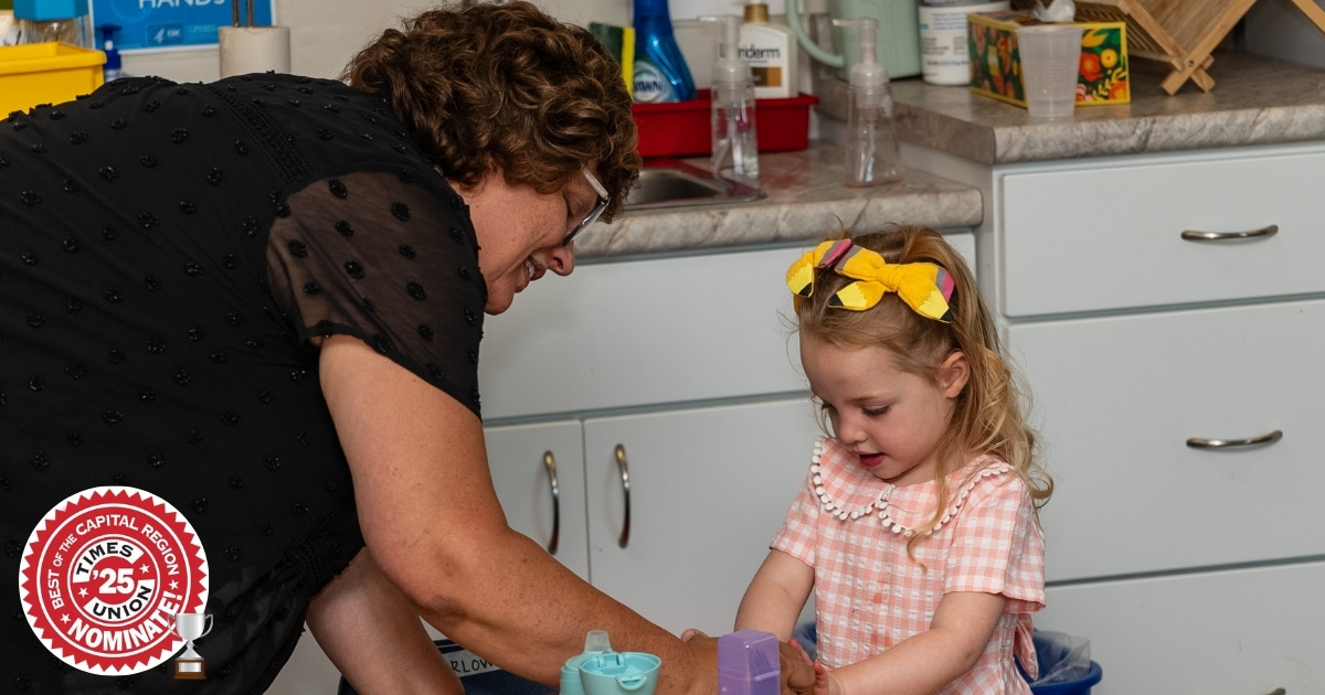 Saint Gregory's Pre-K3 assistant Mrs. Planz helping a young learner with her lunch